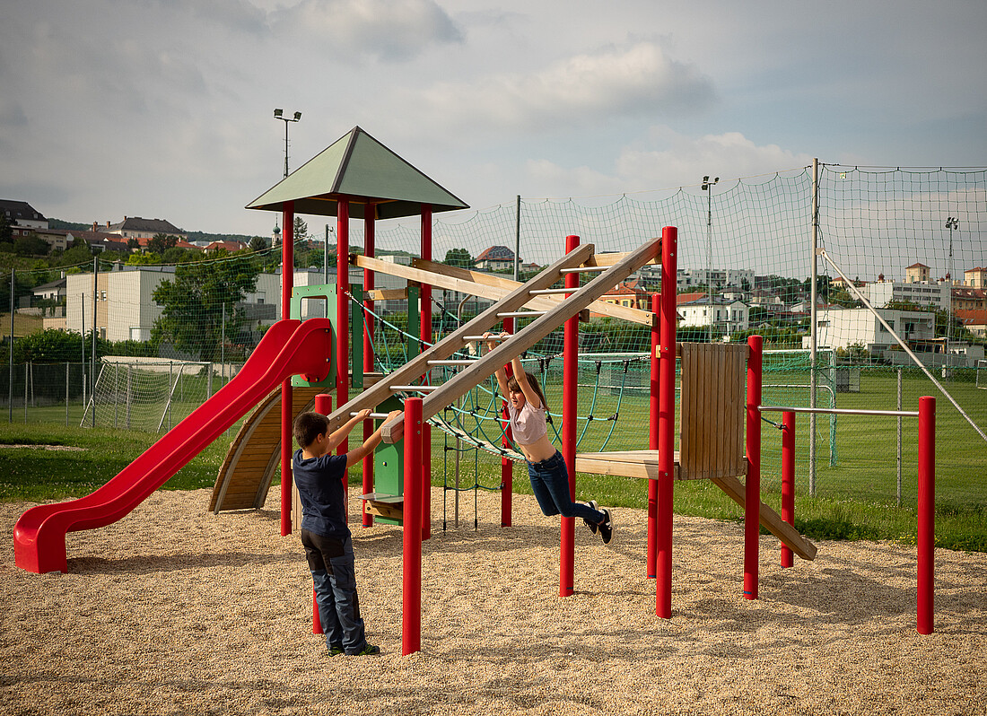 Buntes Klettergerüst mit drei Kindern auf einem Spielplatz im Freien.