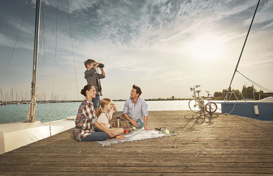 Eine Frau und ein Mann sitzen mit zwei Kindern am Steg eines Sees