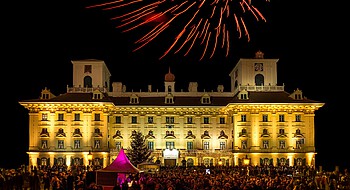 Große Menschenmenge vor beleuchtetem Schloss in der Nacht mit Feuerwerk
