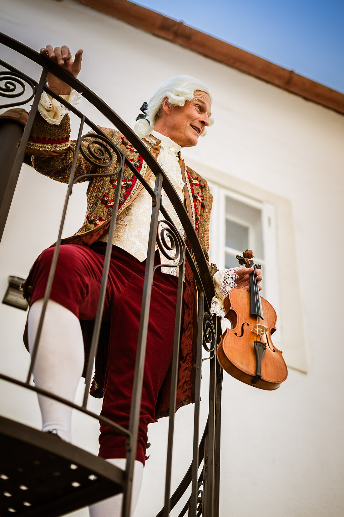 Mann in barockem Kostüm und Geige steht auf einer Wendeltreppe