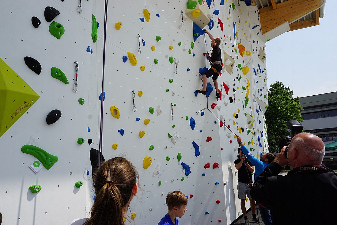 Eine Person klettert auf ein Kletterwand, mehrere Personen sehen zu.