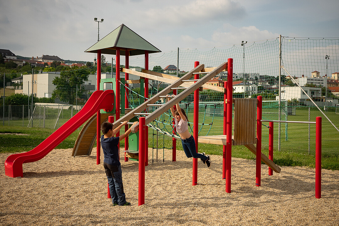 Buntes Klettergerüst mit drei Kindern auf einem Spielplatz im Freien.