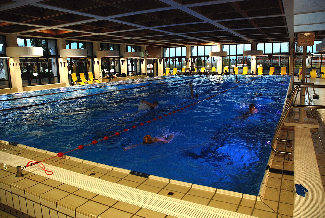 Großes Schwimmbecken in einem Hallenbad mit Schwimmern und Liegestühlen
