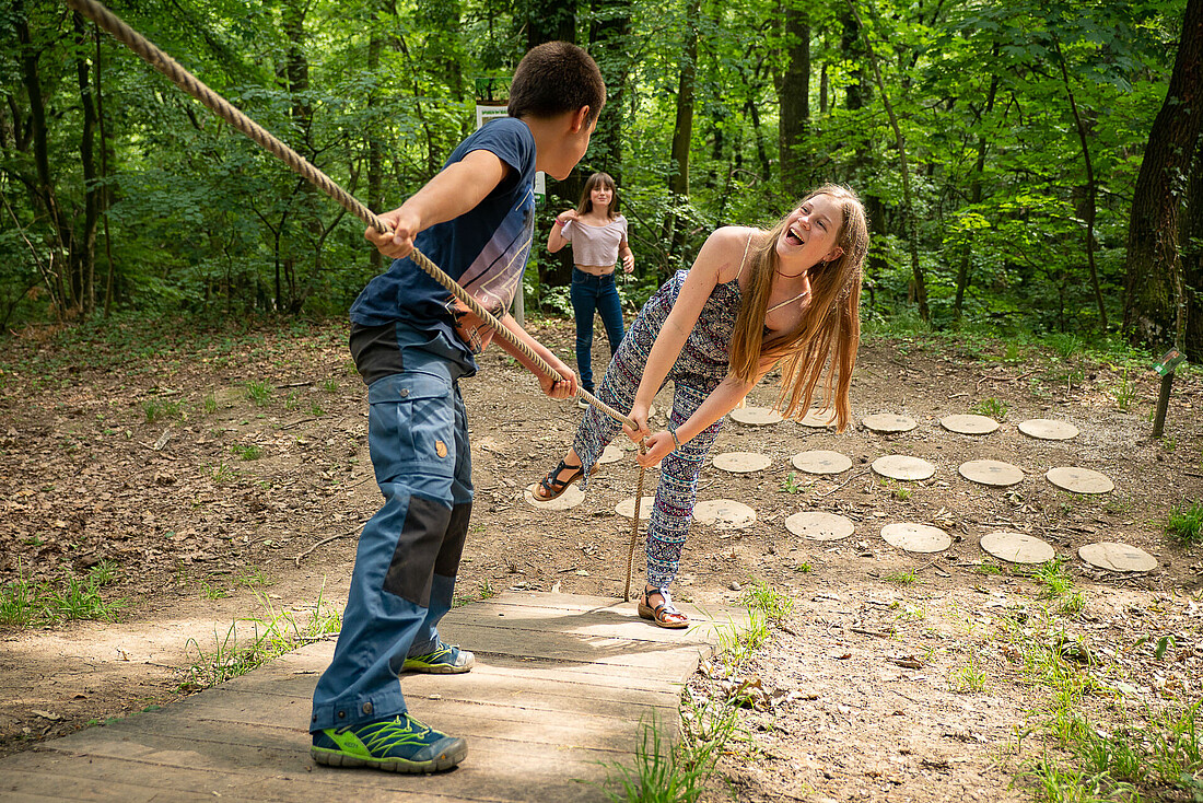 Ein Bub zieht ein Mädchen an einem Seil über eine schräge Holzplatte.