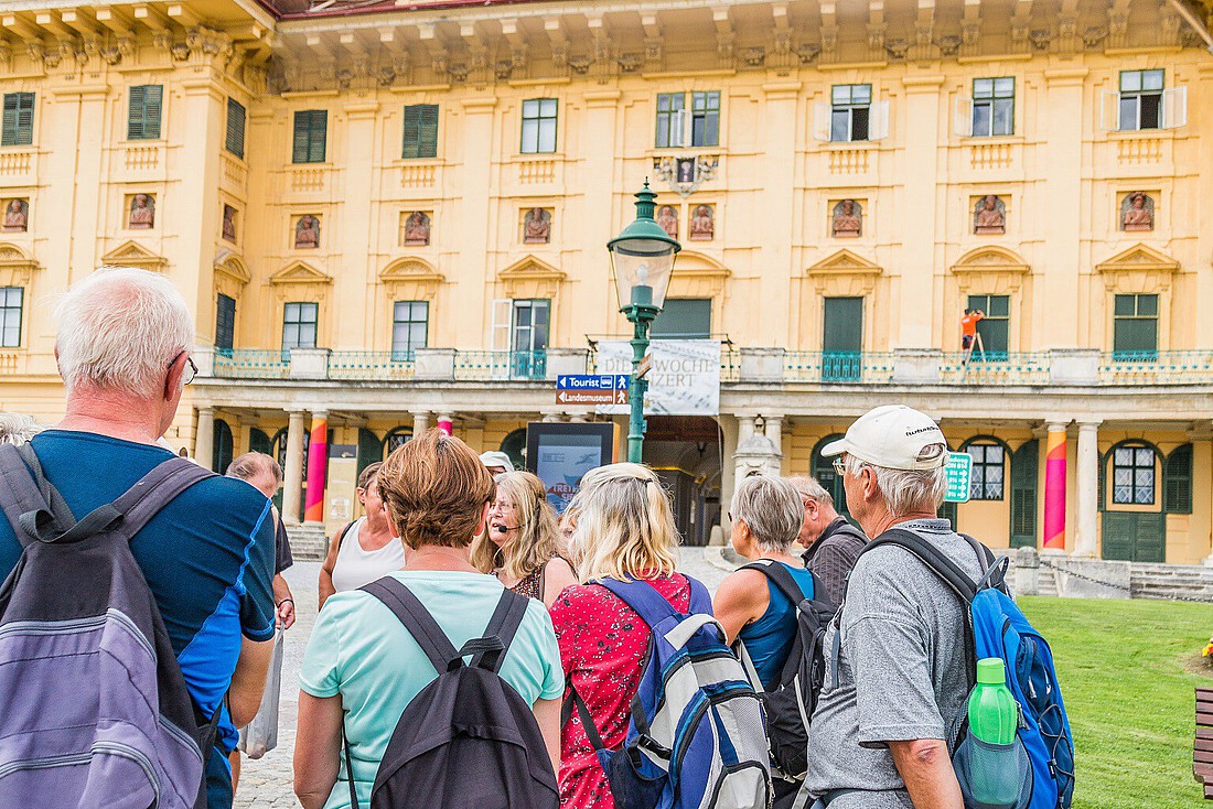 Eine Touristengruppe mit Guide steht vor einem gelben Barockschloss