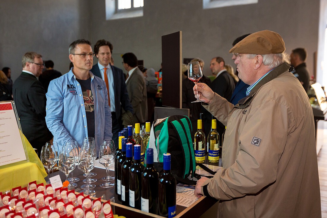 Älterer Mann mit Weinglas in der Hand verkauft Weine in einer Markthalle an Kunden