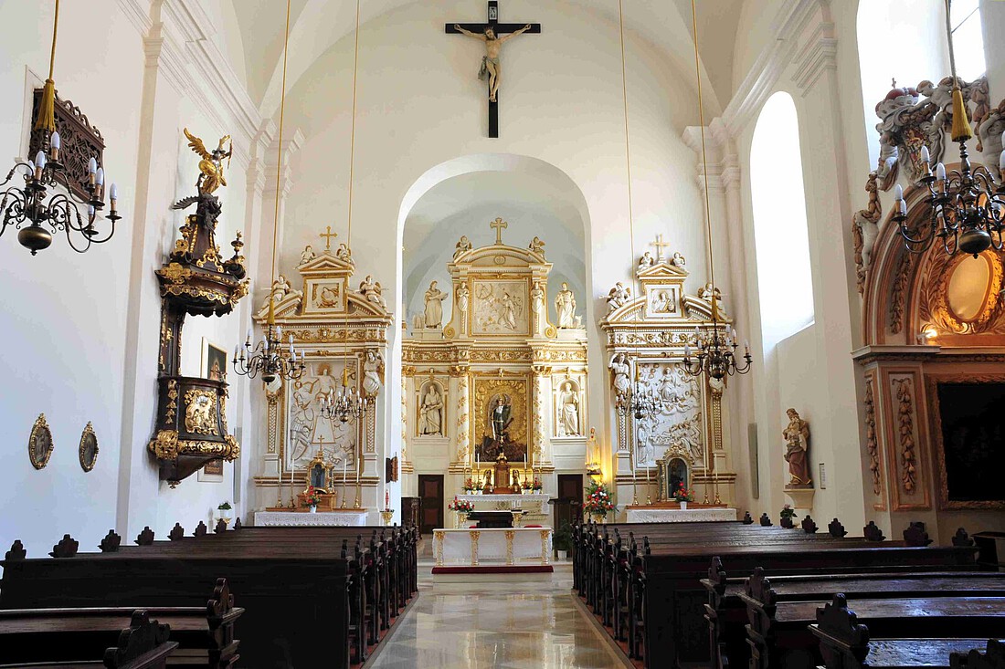 Innenraum einer barocken Kirche mit dunkelbraunen Bänken und goldenen Hochaltar.