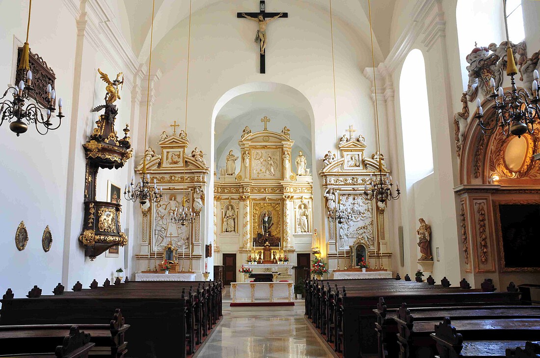 Innenraum einer barocken Kirche mit dunkelbraunen Bänken und goldenen Hochaltar.