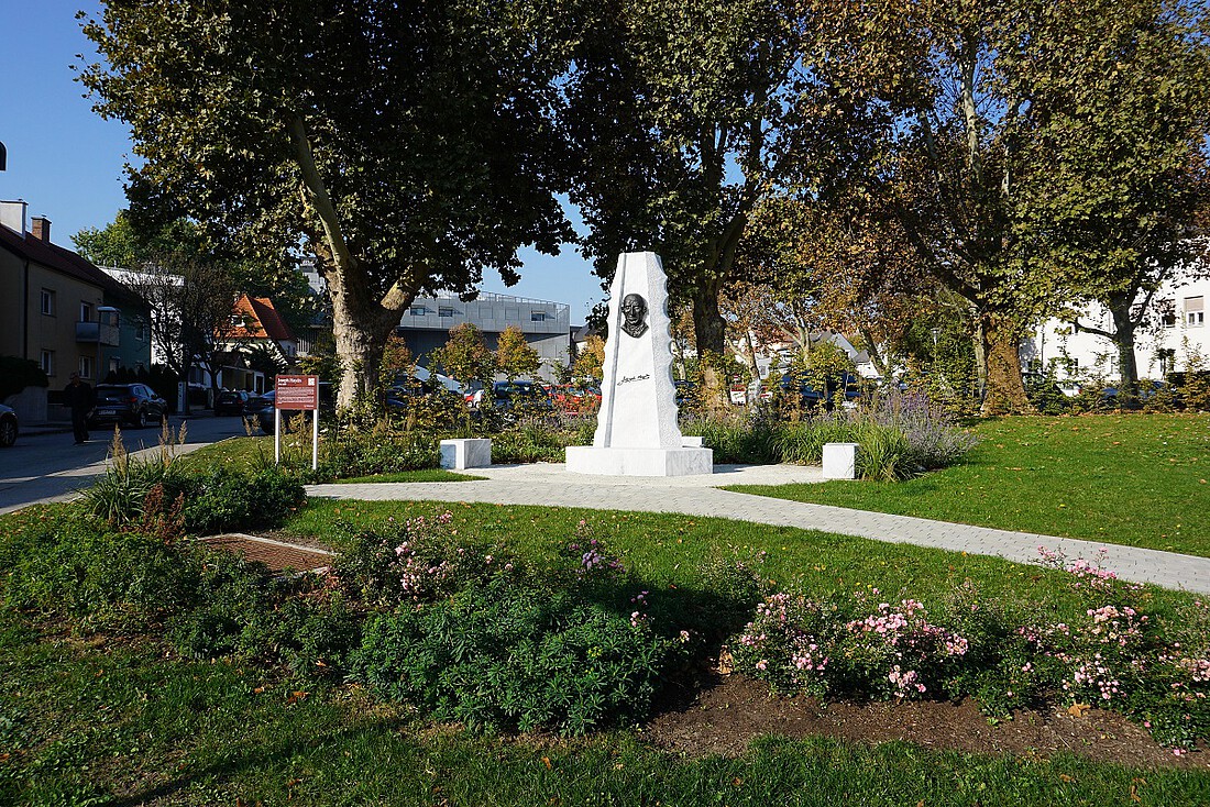 Hohes, quaderförmiges Denkmal aus weißem Marmor in einem Blumenbeet