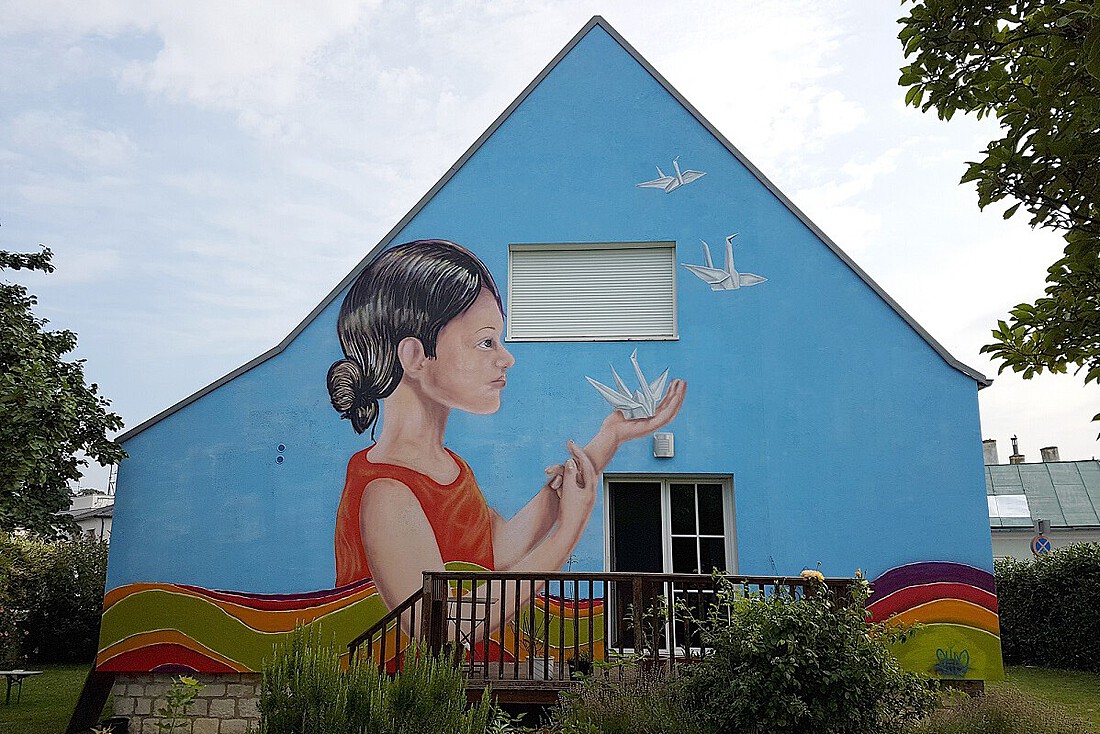 Älteres, kleines Haus, dessen Fassade blau ist mit Porträt einer Frau und Vögel.