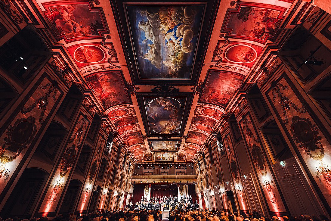 Ein in rotes Licht getauchter Konzertsaal mit barockem Deskenfresken