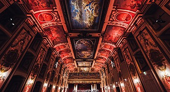 Ein in rotes Licht getauchter Konzertsaal mit barockem Deskenfresken
