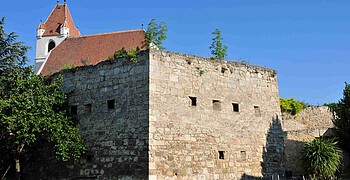 Gut erhaltener Teil einer mittelalterlichen Stadtmauer mit Kirchendach im Hintergrund