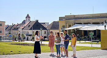 Guide steht mit ein paar Leuten am Schlossplatz mit Blick auf Fußgängerzone und das Restaurant Henrici