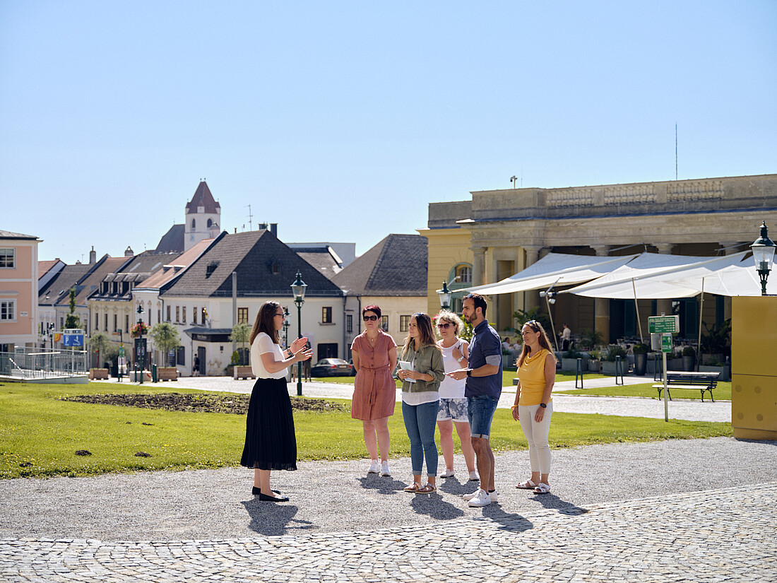 Guide steht mit ein paar Leuten am Schlossplatz mit Blick auf Fußgängerzone und das Restaurant Henrici