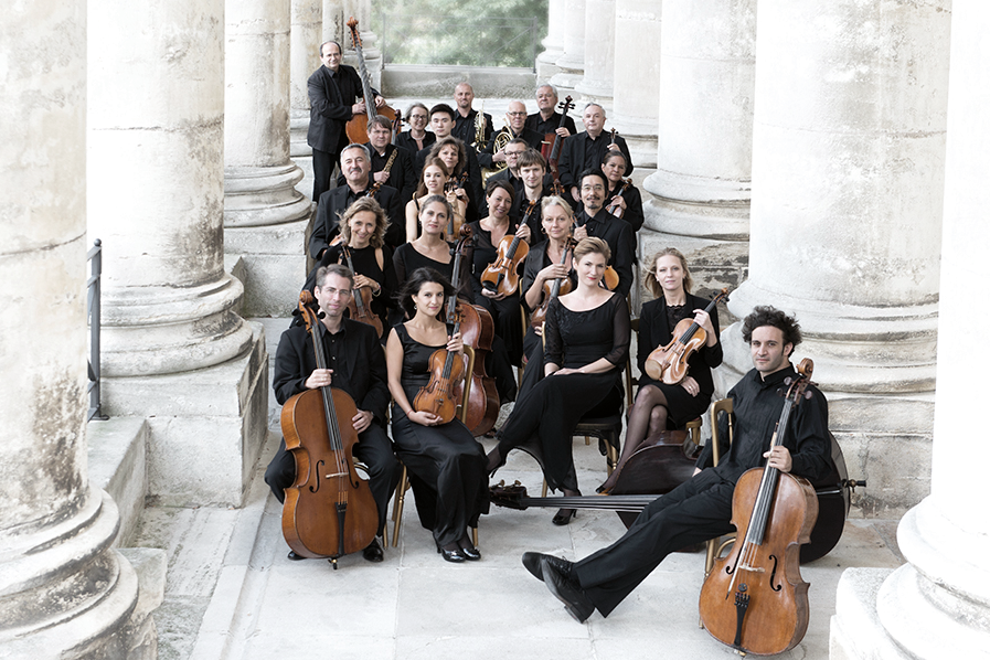 Männer und Frauen eines Orchesters mit Musikinstrumenten auf historischem Portikus.