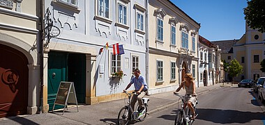 Ein Mann und eine Frau fahren mit Fahrrändern an barocken Häusern vorbei