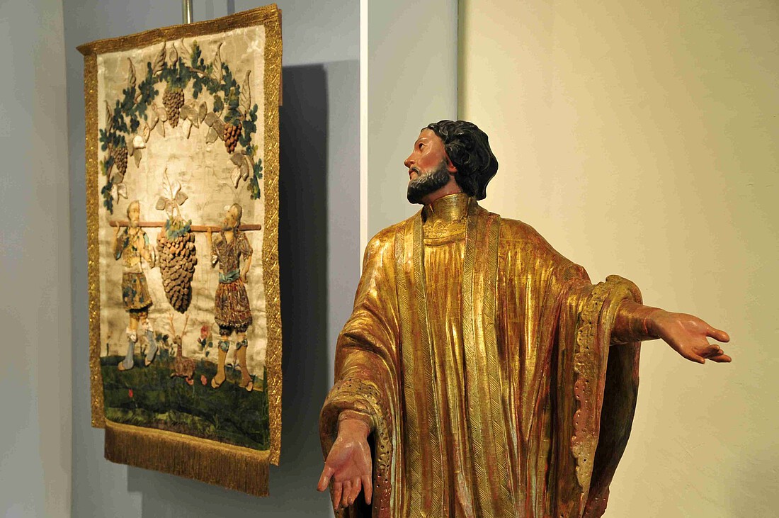 Heiligenfigur in goldenem Gewand vor einem Bild