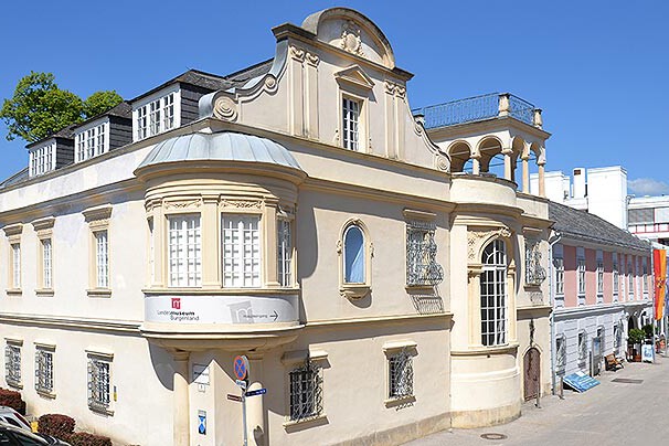 Großes barockes, weißes Haus mit rundem Erker an der Front im ersten Stock.