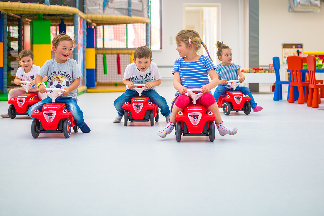 Fünf Kinder auf roten Bobbycars