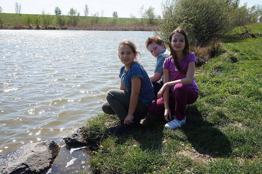 Zwei Mädchen und ein Bub am Ufer eines Baches