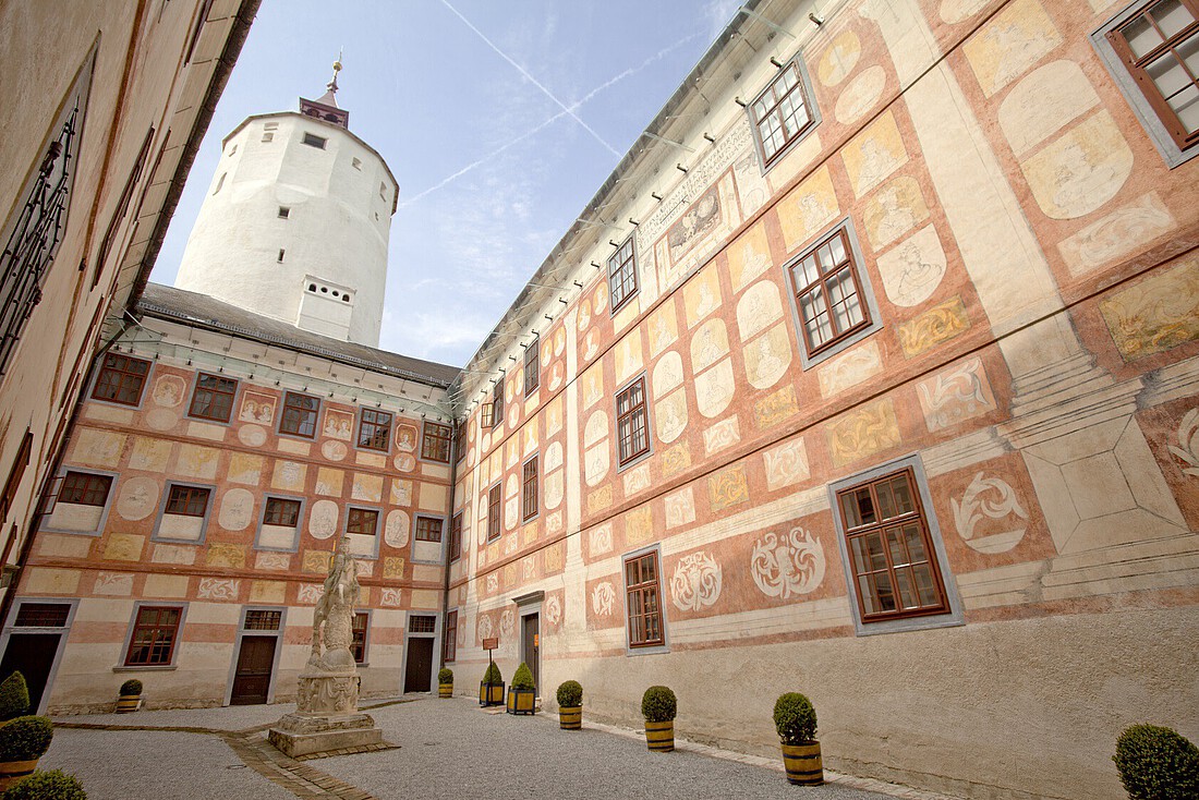 Innenhof einer Burg mit braunen Wandfresken und Turm im Hintergrund.