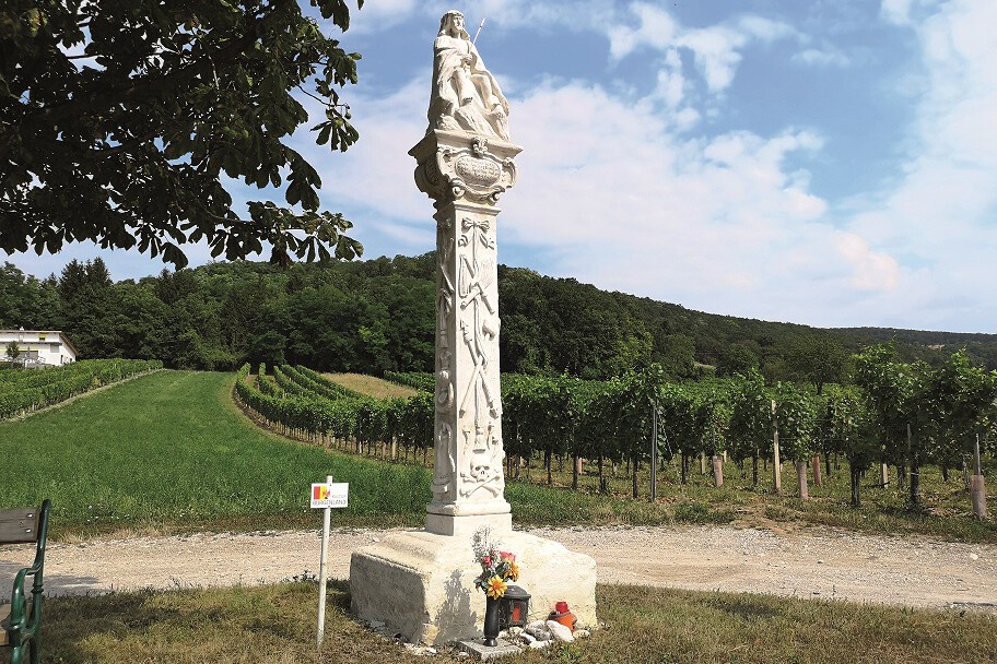 Steinerner Bildstock auf einer Säule vor Weingärten.