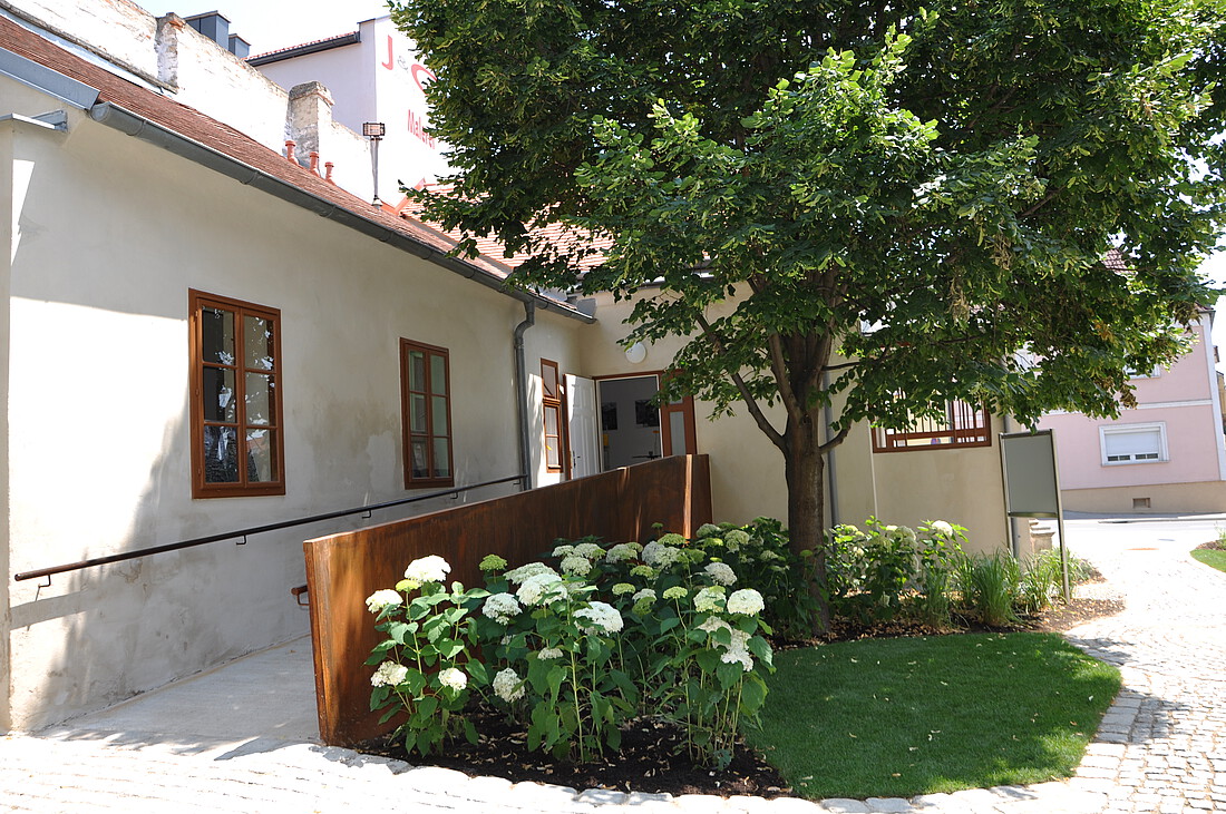 Kleines, altes, weißes Haus mit weißen Blumen und Baum davor