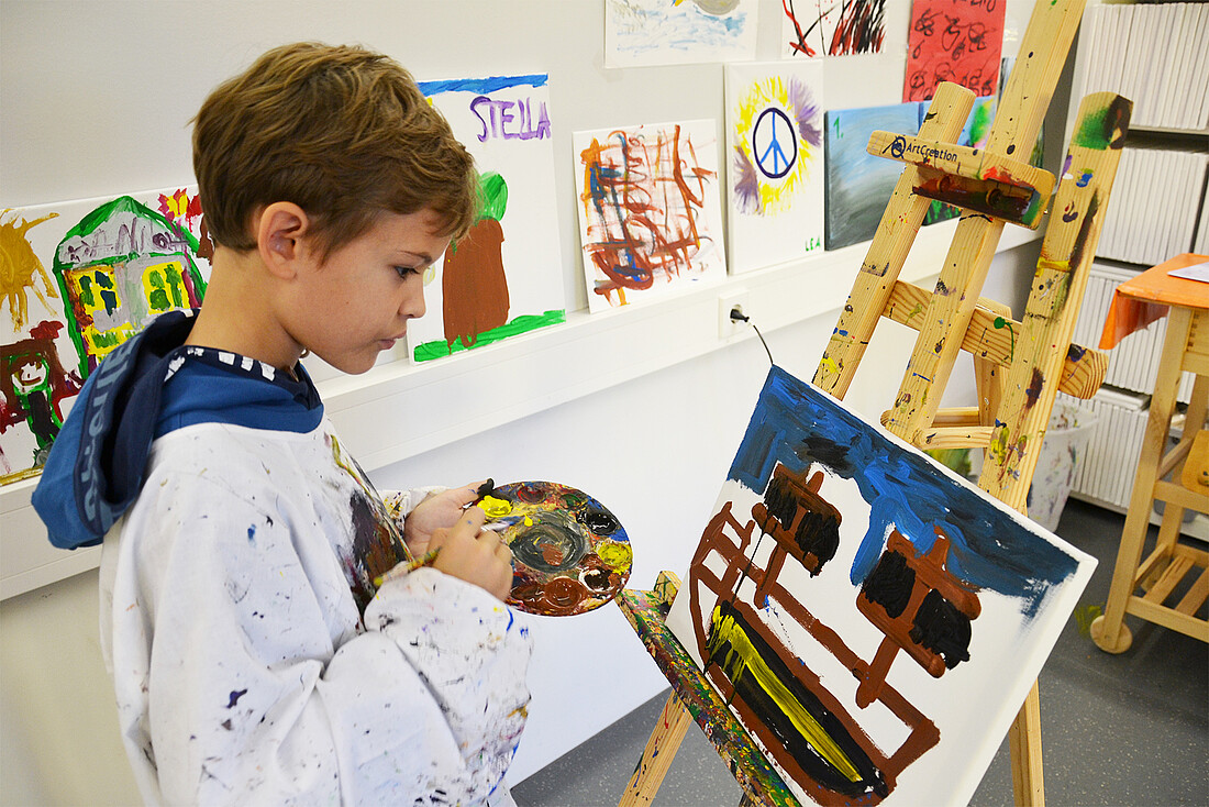 Ein Junge in Malerkittel malt ein Bild auf einer Staffelei