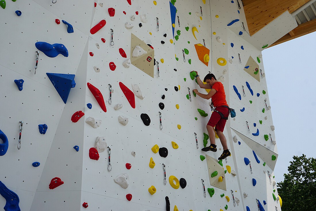 Mann kletter auf eine weiße Kletterwand mit bunten Griffen hinauf