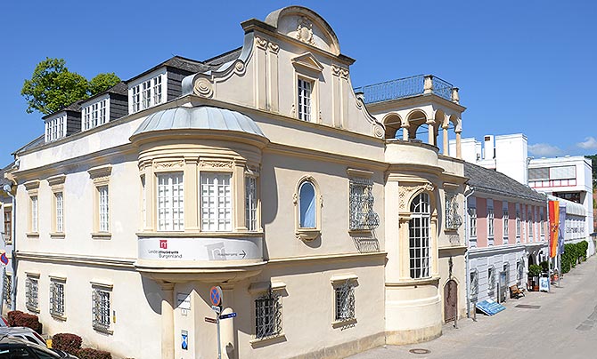 Großes barockes, weißes Haus mit rundem Erker an der Front im ersten Stock.